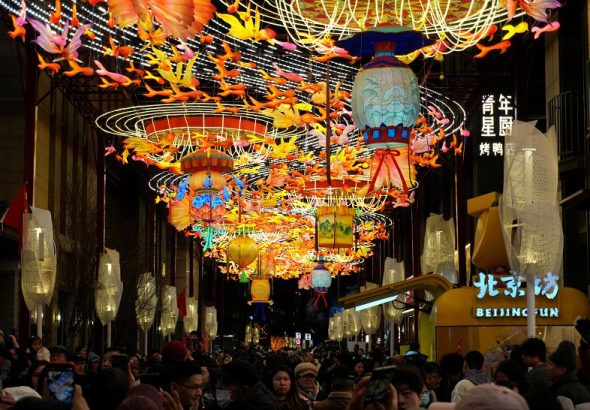 2月18日，位於北京前門大街旁的廊房頭條，遊客在花燈下拍照。春節期間，北京前門步行街及周邊商圈各式花燈流光溢彩，吸引眾多遊客前來打卡拍照。 中新社