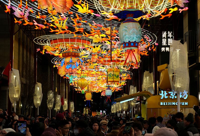 2月18日，位於北京前門大街旁的廊房頭條，遊客在花燈下拍照。春節期間，北京前門步行街及周邊商圈各式花燈流光溢彩，吸引眾多遊客前來打卡拍照。 中新社