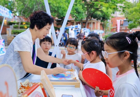 6月13日，國家級非物質文化遺產代表性項目永春紙織畫代表性傳承人方碧雙（左）在非遺市集向小朋友展示紙織畫文創產品。　中新社