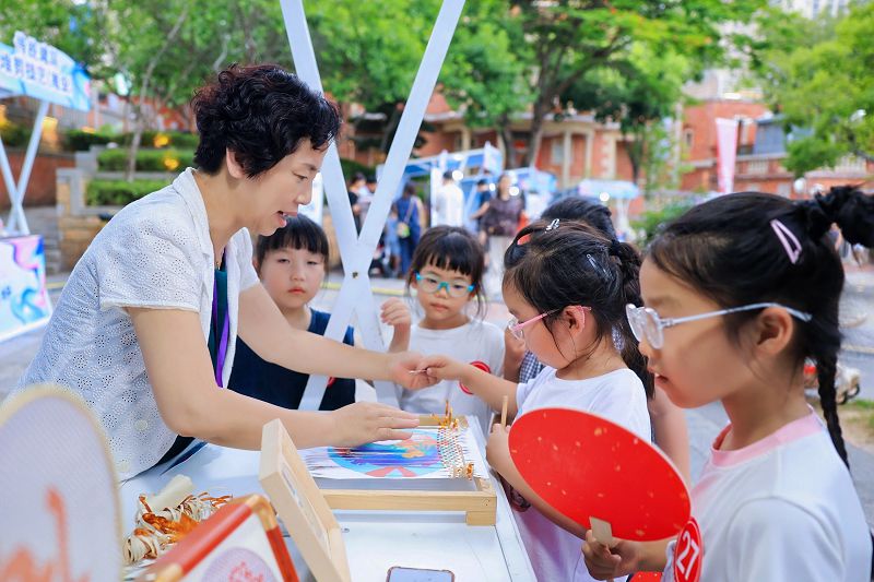6月13日，國家級非物質文化遺產代表性項目永春紙織畫代表性傳承人方碧雙（左）在非遺市集向小朋友展示紙織畫文創產品。　中新社