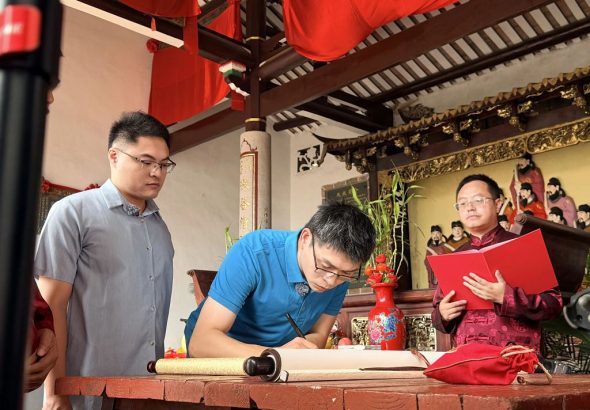 ▲在林彥辰（左一）的陪同下，林冠廷（左二）執筆在《入譜歸宗》登記冊上填寫信息