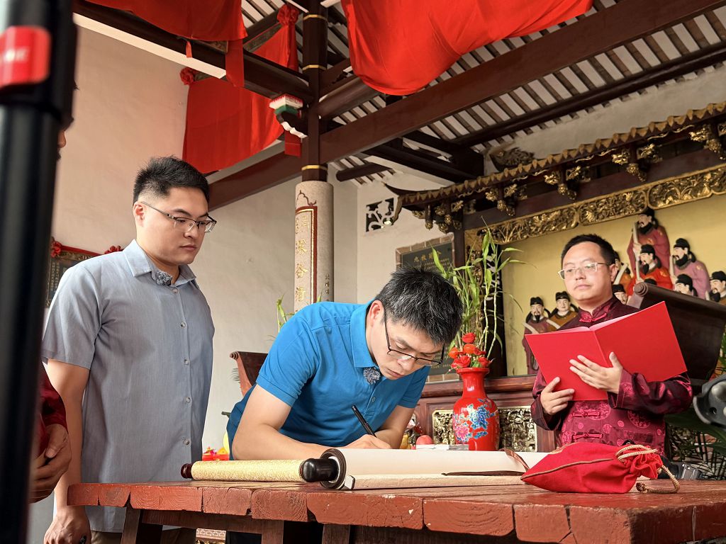 ▲在林彥辰（左一）的陪同下，林冠廷（左二）執筆在《入譜歸宗》登記冊上填寫信息